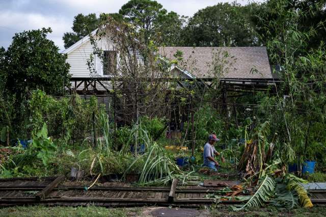 A man works near a storm damaged house with plant debris everywhere