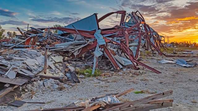 A collapsed structure is surrounded by debris at sunset.