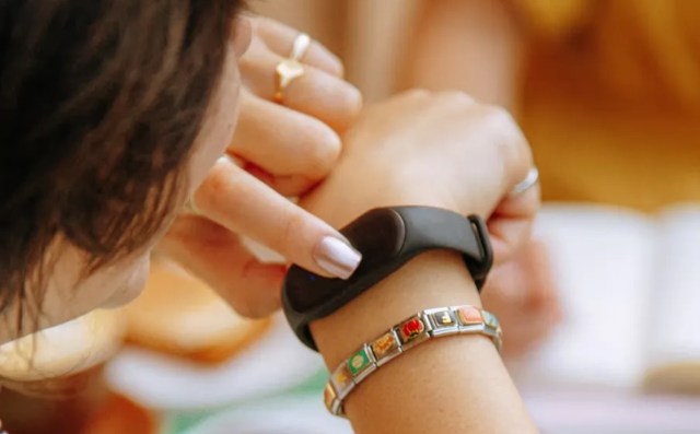 A person looks at a smartwatch while wearing a colorful bracelet on their wrist.