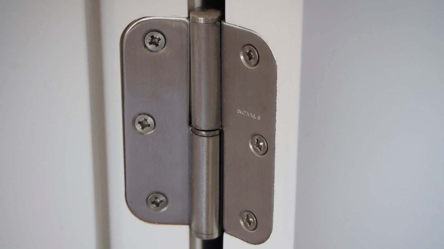 A metal door hinge attached to a white door.