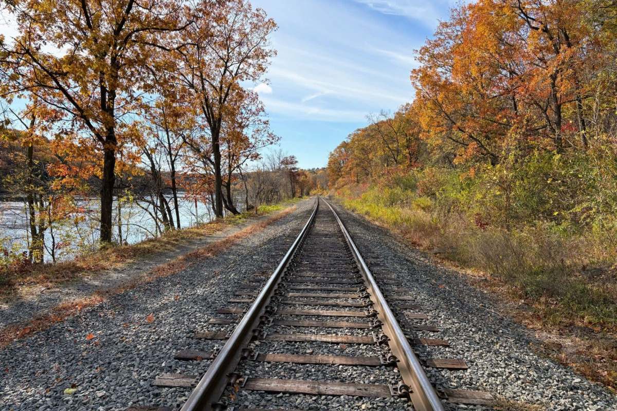 A railway track surrounded by trees with autumn foliage and a river in the background.