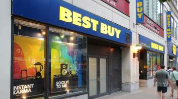 A Best Buy store with colorful window displays and pedestrians walking by.