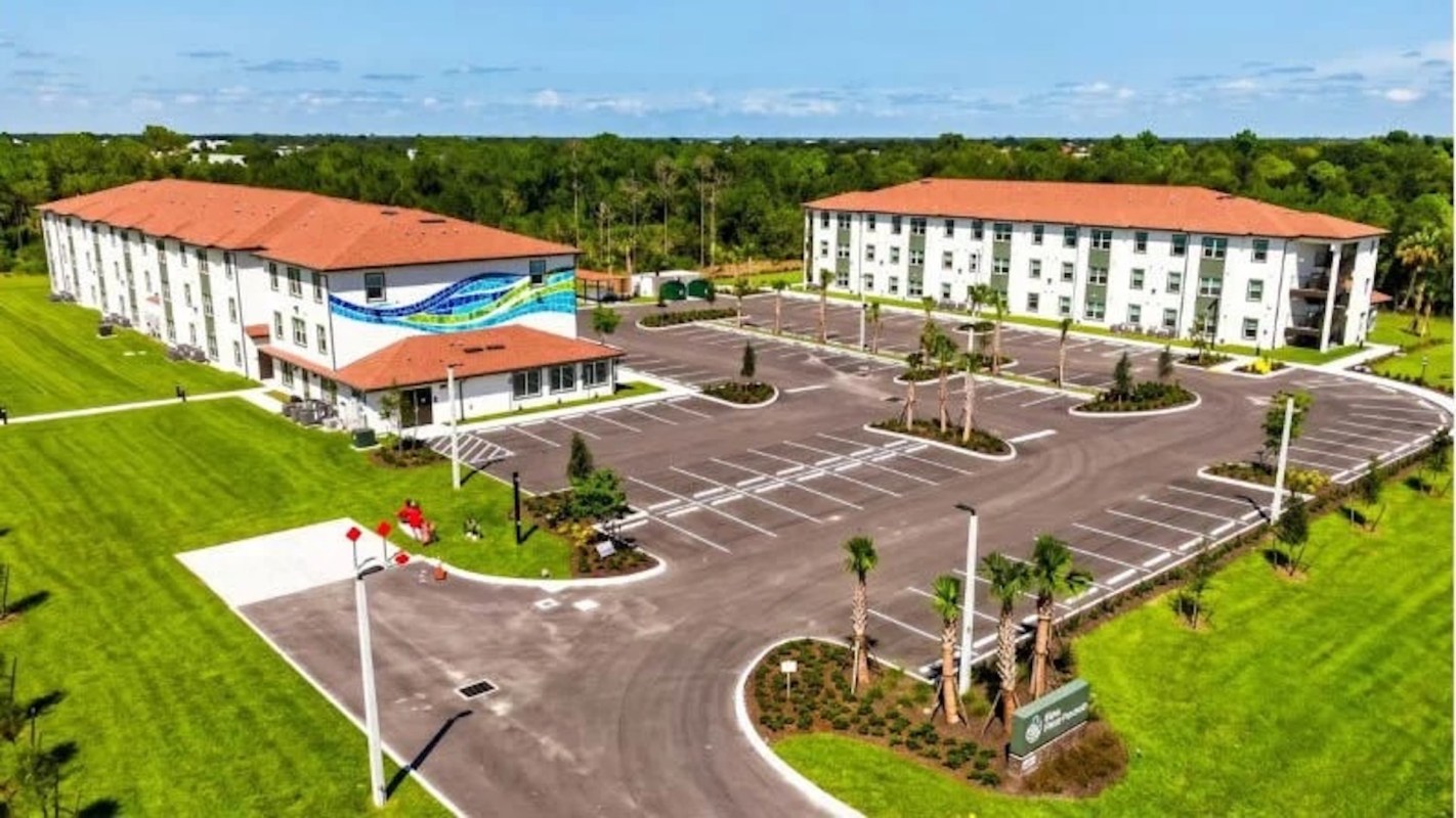 A newly constructed apartment complex with a modern design and landscaped parking area in a green setting.