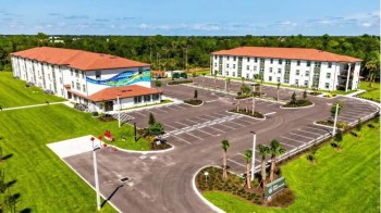A newly constructed apartment complex with a modern design and landscaped parking area in a green setting.