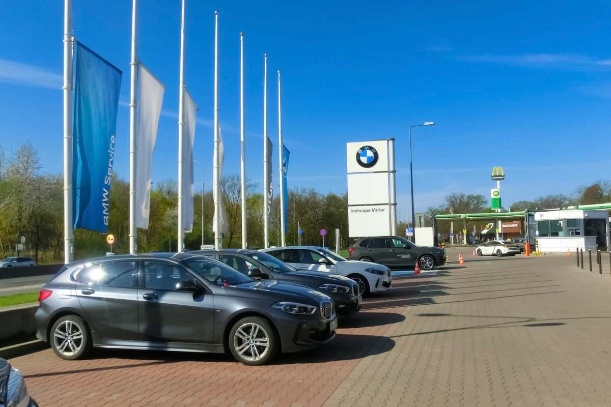 A BMW dealership with parked cars, flags, and a McDonald's in the background.