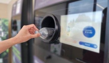 A person deposits a plastic bottle into a recycling machine with a digital screen.