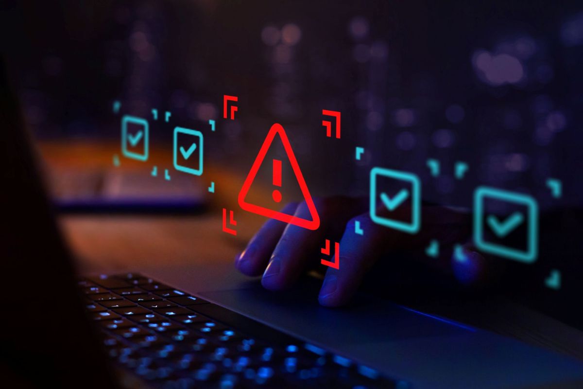 A hand above a laptop, with warning and checkmark icons displayed on the screen.