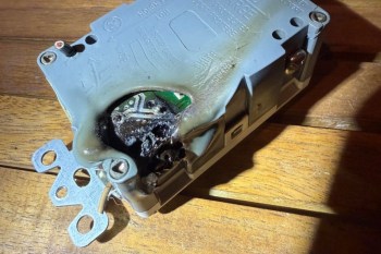 A damaged electrical component with burn marks on a wooden surface.