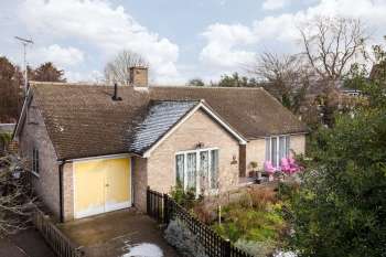 A house with a yellow garage door, two pink chairs on the porch, and a garden with various plants.