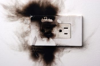 A burnt electrical outlet with black marks and discoloration on the surrounding wall.