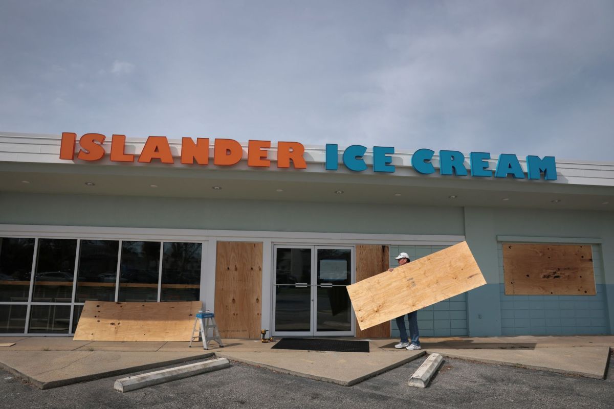 A person putting boards on windows at an ice cream shop.
