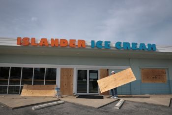 A person putting boards on windows at an ice cream shop.