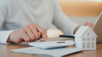 A person using a calculator with a pencil and a model house on a desk.