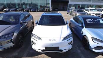 A row of parked cars including a white electric vehicle and several other models in a dealership lot.