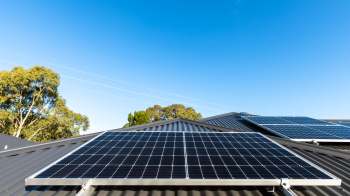 Solar panels installed on a sloped roof with clear blue sky and trees in the background.