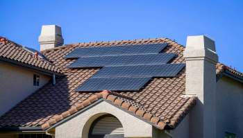 A house roof with several solar panels installed on brown tiled shingles.