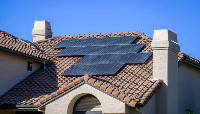 A house roof with several solar panels installed on brown tiled shingles.