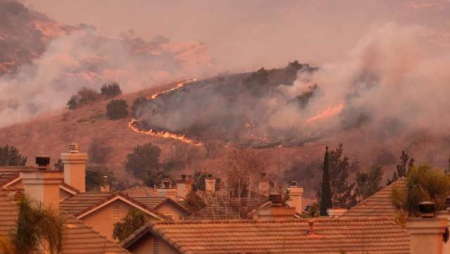 A hillside is engulfed in flames and smoke, with rooftops visible in the foreground.