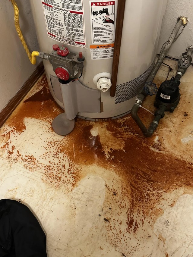 A heat pump water heater surrounded by rust on the floor.