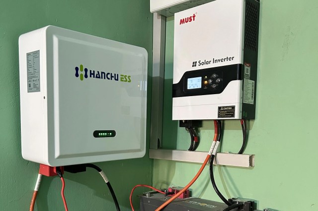 A solar inverter and battery management system mounted on a green wall.