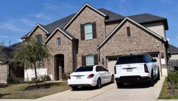 A two-story house with luxury cars in the driveway.