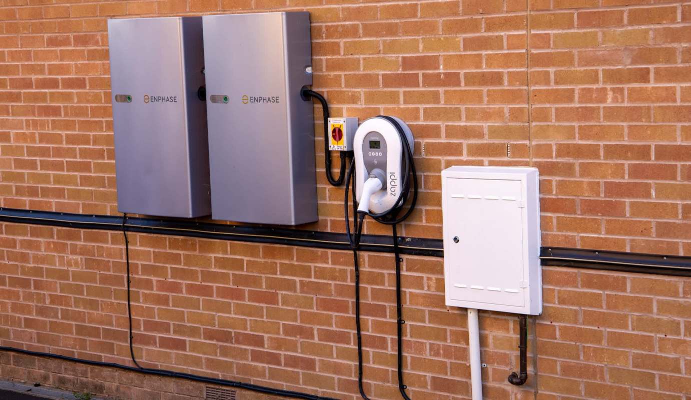 Two energy storage units and an electric vehicle charger mounted on a brick wall.
