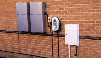 Two energy storage units and an electric vehicle charger mounted on a brick wall.