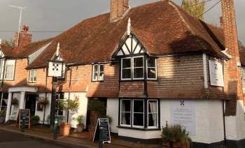 A traditional English building with dark wood accents and a thatched roof, featuring a sign for a local pub.