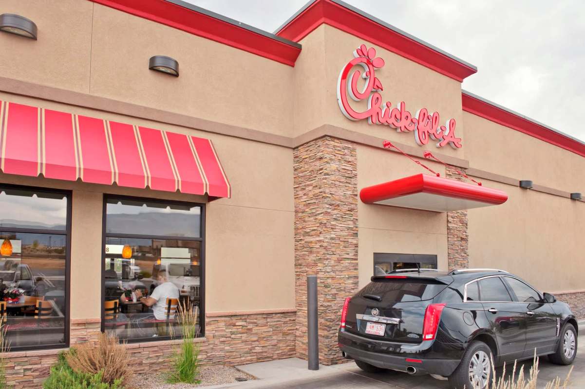 A Chick-fil-A restaurant with a red awning and a black car in the drive-thru.