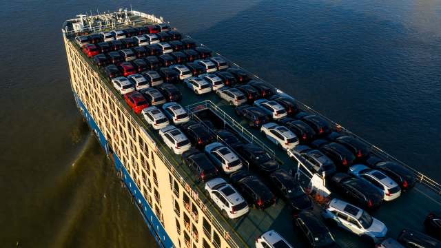 A large cargo ship loaded with numerous cars on its deck navigating through the water.