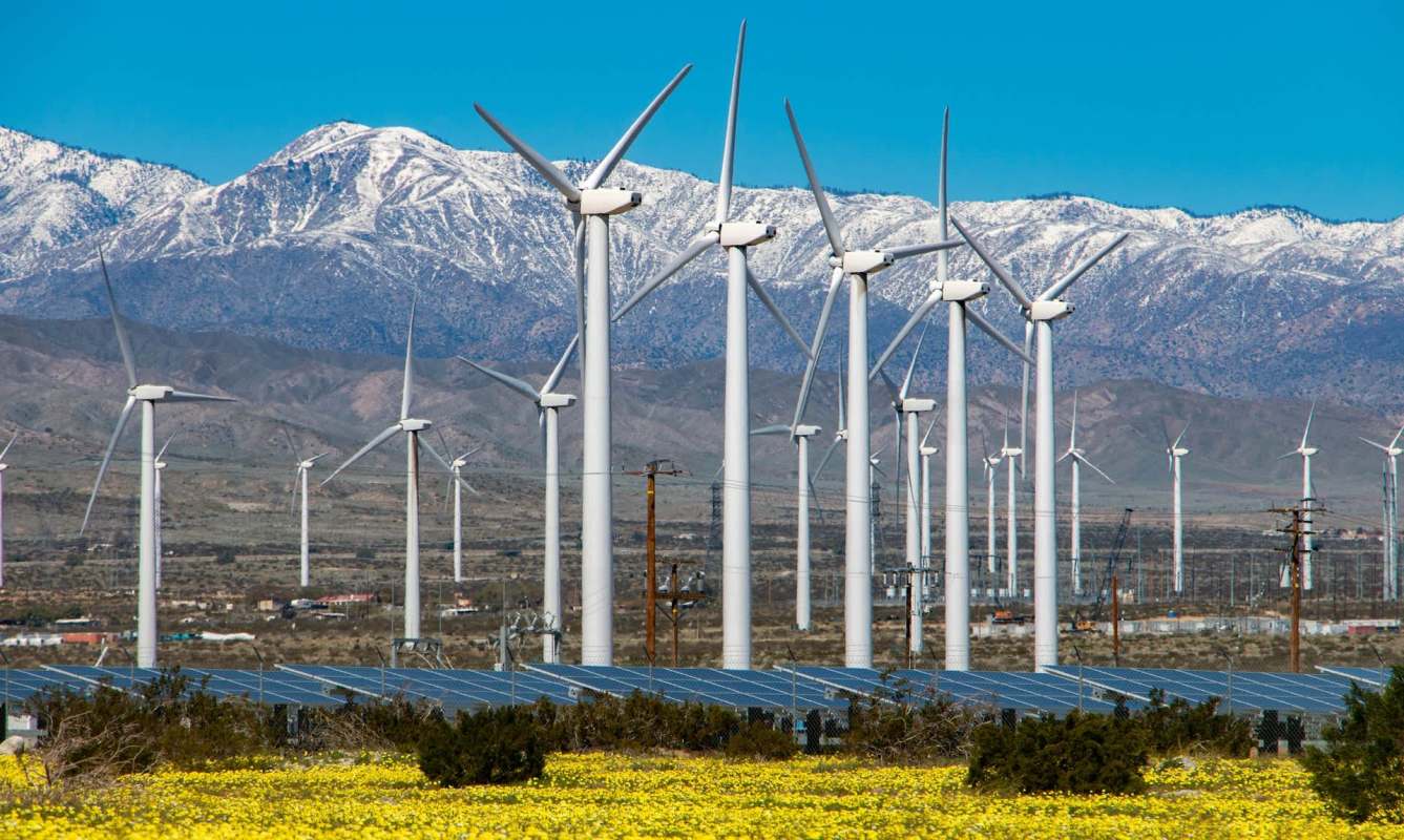 A wind and solar farm in front of snow-capped mountains.