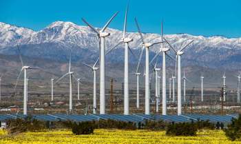 A wind and solar farm in front of snow-capped mountains.