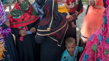 A group of women wearing colorful scarves gathers with children outdoors.