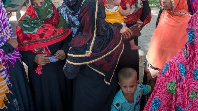 A group of women wearing colorful scarves gathers with children outdoors.
