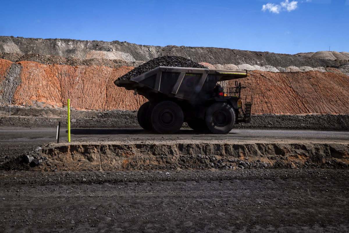 A large dump truck transports coal beside a terraced pile of earth materials in a mining area.