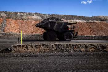 A large dump truck transports coal beside a terraced pile of earth materials in a mining area.