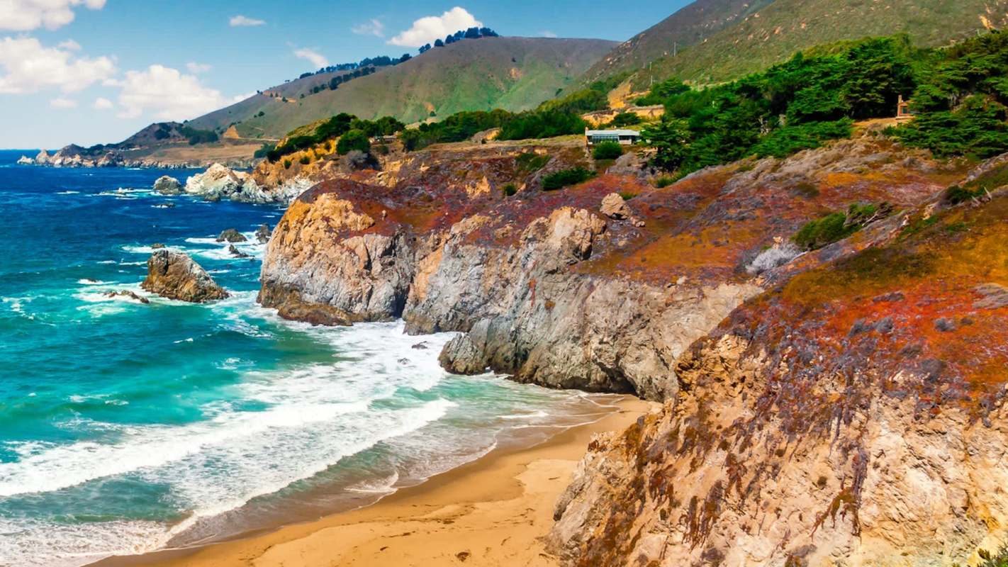A coastal landscape featuring rocky cliffs, sandy beaches, and turquoise waters.