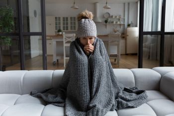 A woman with a beanie and blanket sitting on a couch.