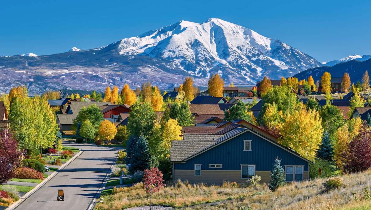 A residential neighborhood with colorful trees and a snow-capped mountain in the background.