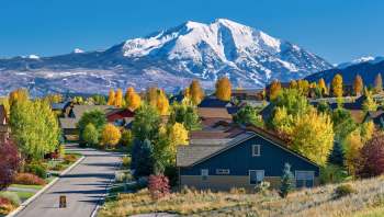 A residential neighborhood with colorful trees and a snow-capped mountain in the background.