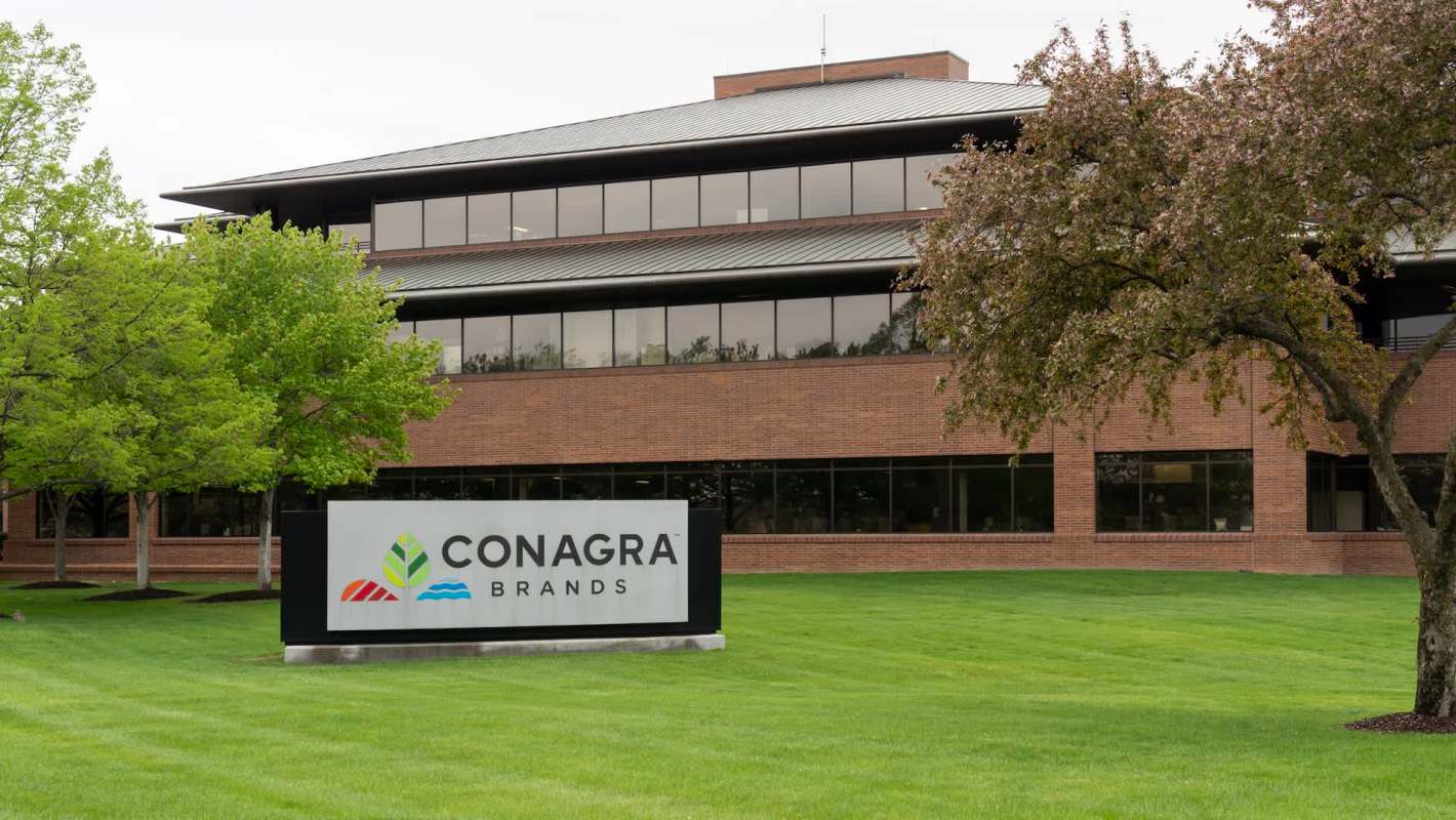 A building with a sign that reads "Conagra Brands" surrounded by green grass and trees.