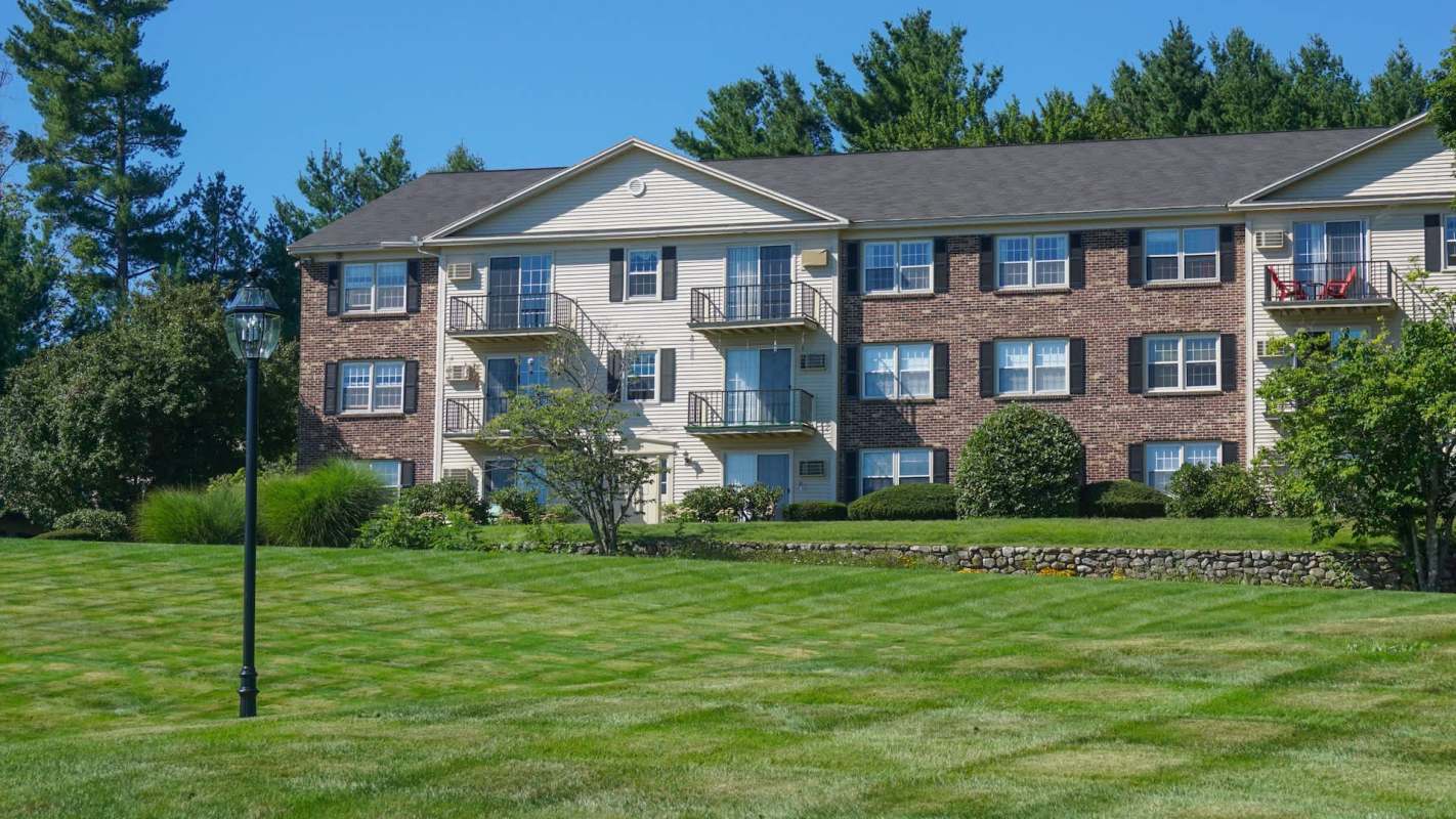 A three-story residential building with a landscaped lawn and a lamppost in front.