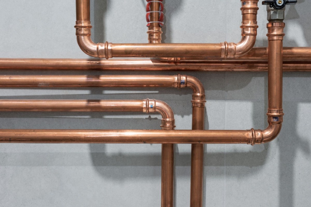 Copper pipes arranged on a wall, featuring various fittings and connections.