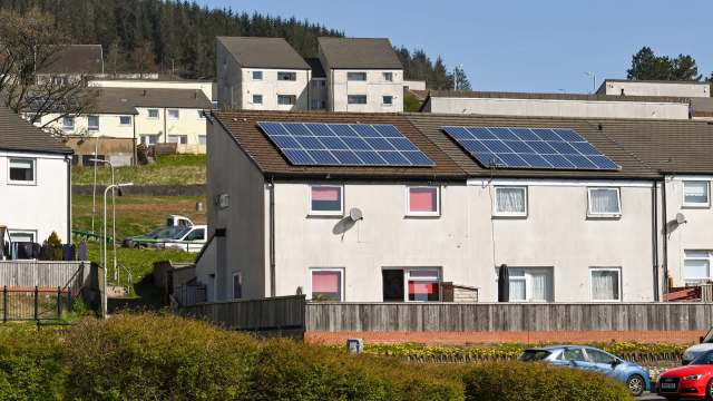 A residential building in Wales with solar panels on the roof and parked cars in the foreground.