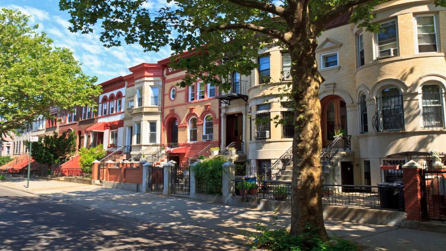 A row of residential buildings with steps and decorative facades along a tree-lined street.