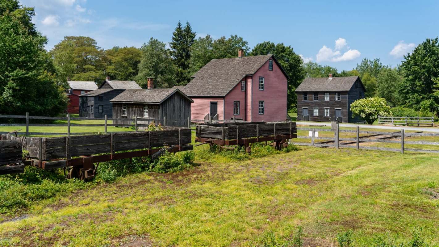 A historical site featuring several wooden buildings and old train cars in a grassy area.
