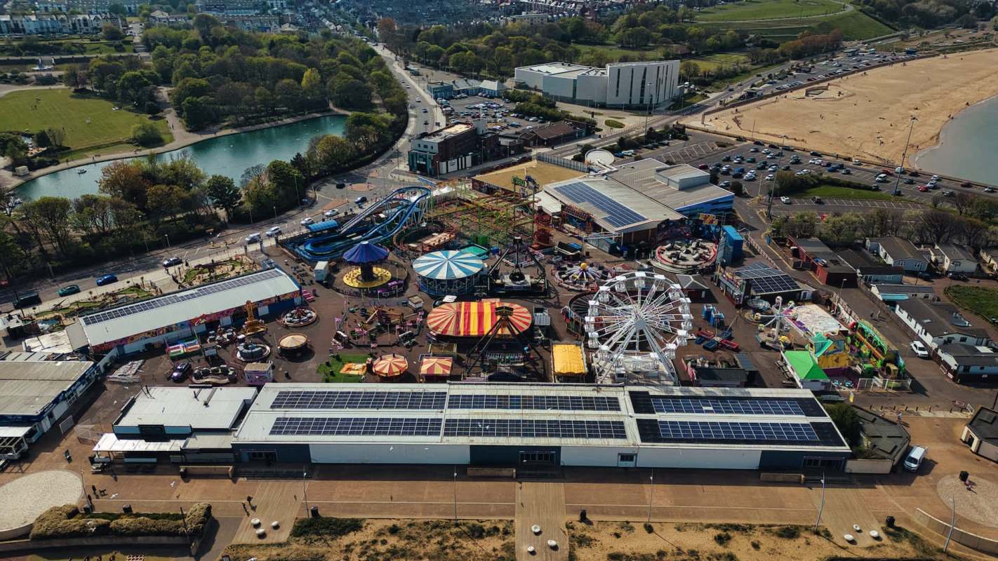 An aerial view of an amusement park with rides, attractions, and surrounding green spaces near a beach.
