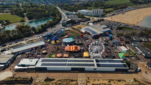 An aerial view of an amusement park with rides, attractions, and surrounding green spaces near a beach.