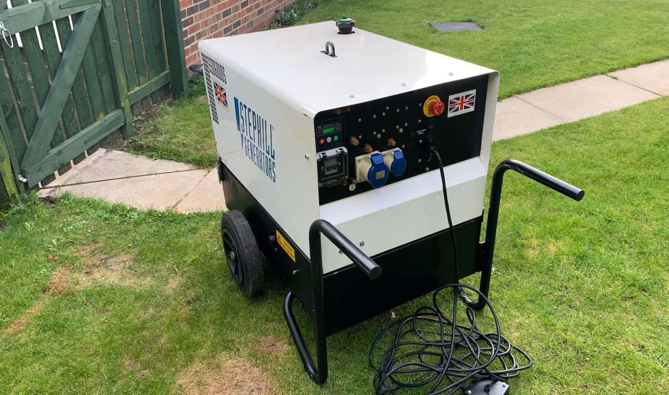 A portable generator on grass near a garden gate.