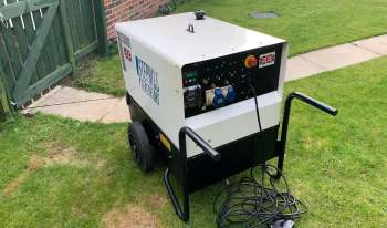 A portable generator on grass near a garden gate.